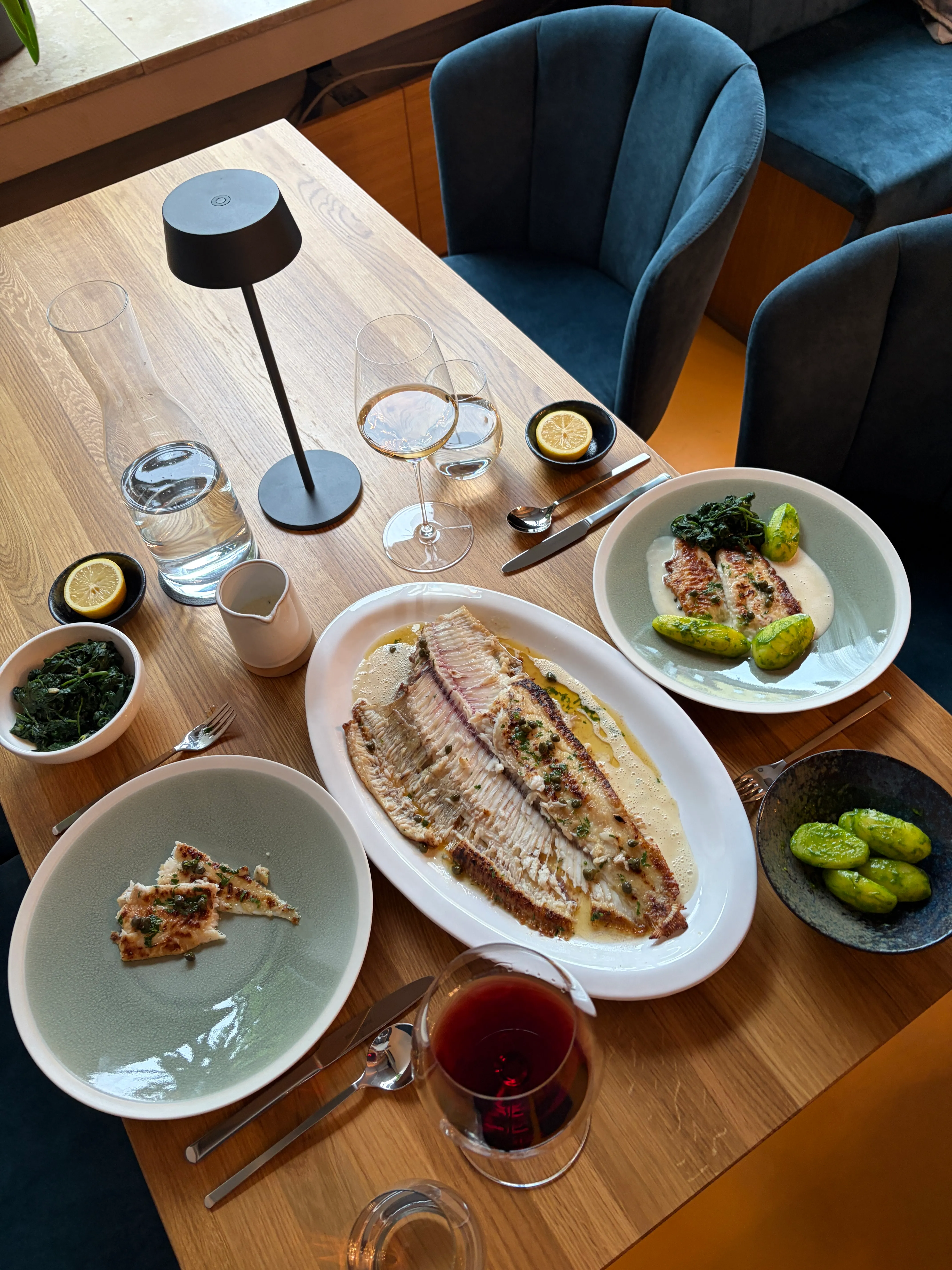Gedeckter Tisch mit ganzer gebratener Seezunge auf der Platte, dazu Kartoffeln, Spinat und Wein